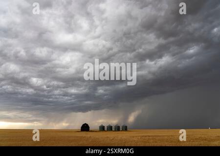 Ominous supercell storm clouds gathering over a farm with grain silos and a barn in the vast plains Stock Photo