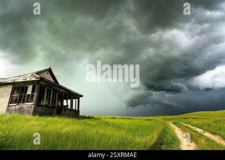Ominous dark clouds gather over an abandoned house in a green field, hinting at an impending storm Stock Photo