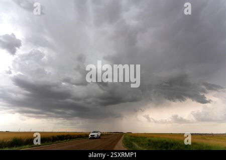 Dark storm clouds are gathering over a vast plain with a car driving on a dirt road Stock Photo