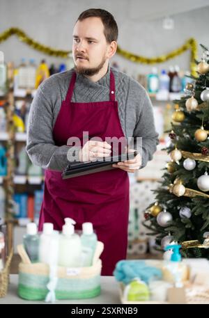 Middle-aged man restocking using tablet in store with New Year decoration Stock Photo