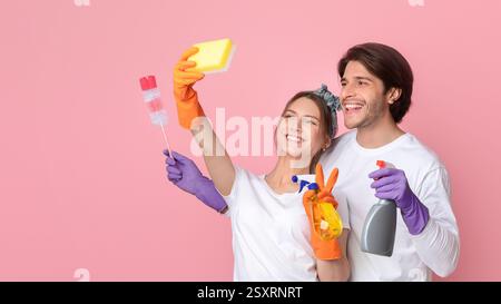 Cleaning Fun. Cheerful millennial couple taking selfie, using sponge like smartphone Stock Photo