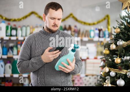 Middle-aged guy scanning QR-code on cleaning spray in store during Christmas Stock Photo