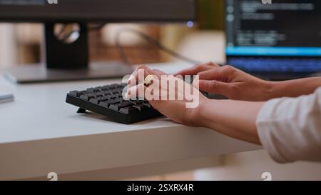 Professional software developer types code on a laptop in a sleek workspace. Asian female freelancer doing remote work on app development, software engineering and agile coding practices. Camera B. Stock Photo