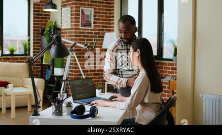 Interracial creative team programing code on a laptop and debugging, using digital tools at home. Professional coders team working on software development and internet security. Camera A. Stock Photo