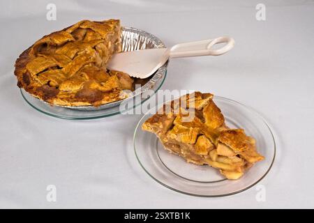 A delicious homemade apple pie with one slice on a glass plate next to a pie cutter. White background. Stock Photo