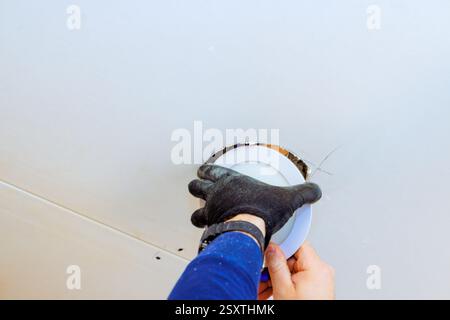 Worker is carefully placing new light fixture into ceiling opening during home improvement task. Stock Photo