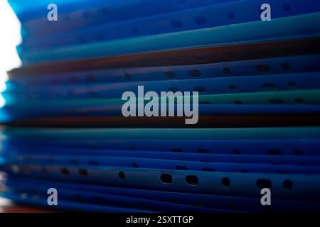 A vibrant collection of plastic folders in various shades of blue is neatly stacked on a desk. The light enhances the colors, creating an organized ye Stock Photo