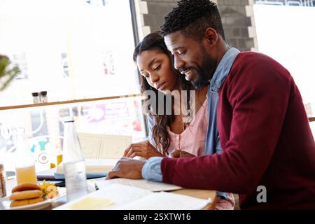 Studying, students and couple with books, restaurant and knowledge for exam in morning or bonding. Happy, education and black people with information Stock Photo