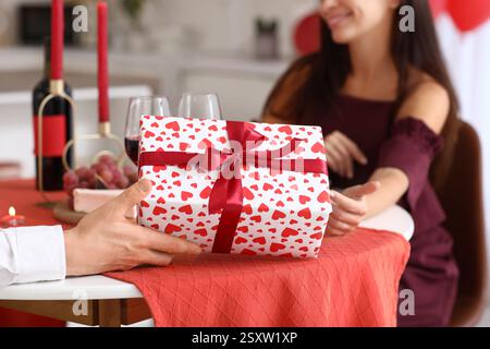 Loving couple exchanging gifts at served dining table in kitchen, closeup. Valentine's Day celebration Stock Photo