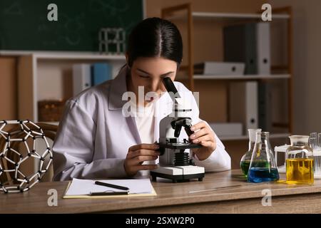 Female inventor looking through microscope at table in laboratory Stock Photo