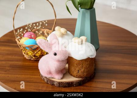 Easter cakes with rabbit and wicker basket of colorful eggs on table in living room Stock Photo