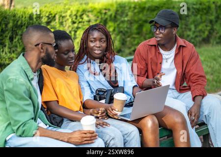 Interracial friends group enjoying coffee in park with laptops, chatting, relaxing and freelancing Stock Photo