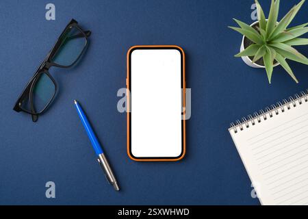 Blank screen smartphone on blue table. Notepad, pen and glasses around Stock Photo