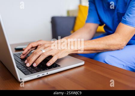 Close up view of senior doctor working on laptop sitting on sofa at home Stock Photo