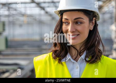 Smiling young female engineer in a hardhat and yellow vest Stock Photo