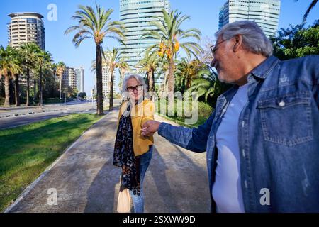 Happy senior couple holding hands walking in a city park with palm trees. Stock Photo