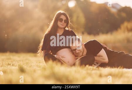 Man embracing his wife. Woman is pregnant. Lovely couple sitting on the field together. Stock Photo