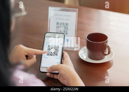 Detail of customer hand making payment through smartphone and scan code at cafe. Asian woman paying with QR code. Back view, selective focus. Stock Photo