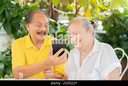Elderly Asian grandfather and grandmother spend time having fun using smartphone apps. Retriement lifestyle concept. Stock Photo