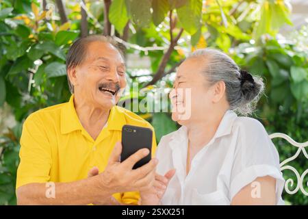 Senior lover enjoying while doing video call via app on phone. Older Asian people having fun at outdoor. Lifestyle concept. Stock Photo