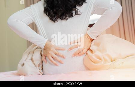 Unhealthy unhappy woman sitting on bed, massaging back, suffering from painful feelings, waking up in morning after sleeping on uncomfortable mattress Stock Photo