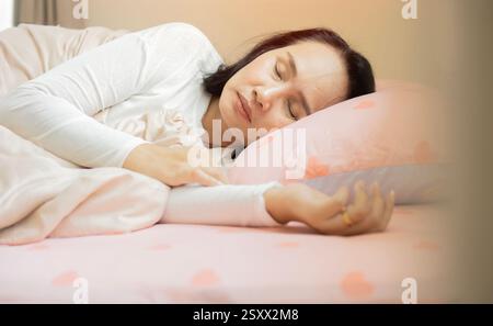 Woman sleeping. High angle view of beautiful young woman lying in bed and keeping eyes closed while covered with blanket. Stock Photo