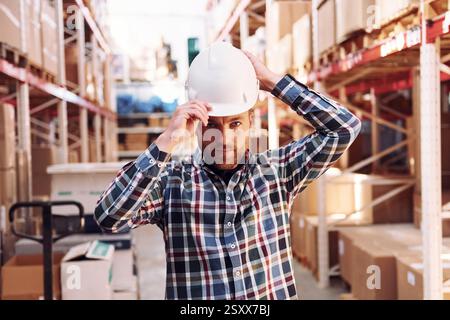Wearing hard hat. Employee in uniform is working in the storage at daytime. Stock Photo