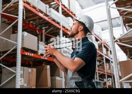 With digital tablet in hands. Employee in uniform is working in the storage at daytime. Stock Photo