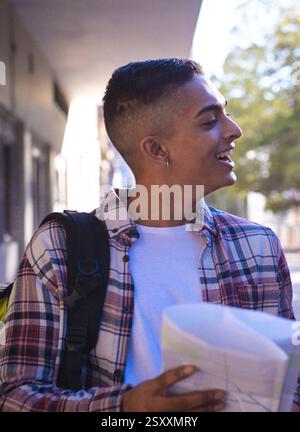 Smiling young man with backpack holding map, exploring city streets Stock Photo