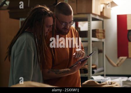 Wide shot of two Caucasian business partners looking at tablets screen and discussing new order of coffee beans Stock Photo