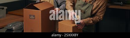 Website banner with high angle shot of unrecognizable workers using sticky tape to pack cardboard boxes with coffee Stock Photo