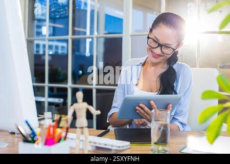 Smiling woman using tablet at office desk with creative tools around Stock Photo
