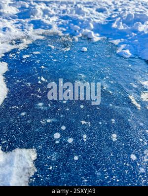 Frozen puddle on a snowy surface, ice patterns and trapped air bubbles. High quality photo Stock Photo