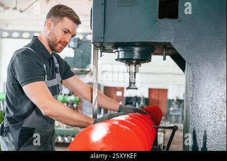 Measuring red colored sharp part. Man in uniform is in workstation developing details of agriculture technique. Stock Photo