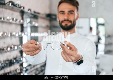 Big choice. Stylish man with beard choosing glasses in the optics store. Stock Photo
