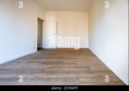 Interior of an empty room with wooden floor and white walls, featuring a open door and white skirting boards Stock Photo