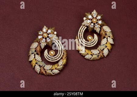 Glamorous antique Golden pair of earrings on red background. Luxury female jewelry, Indian traditional jewellery, kundan earring, Bridal Gold earrings Stock Photo