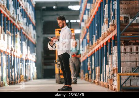 Using tablet to check the products. Storage worker is in the warehouse. Stock Photo