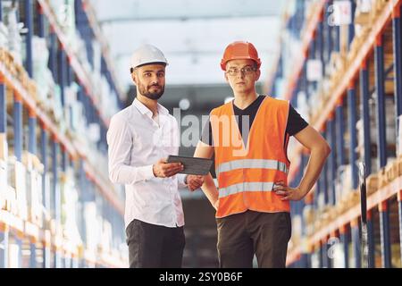 Standing and working together. Two men in storage is in the warehouse. Stock Photo