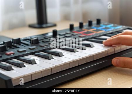 Woman playing MIDI keyboard with control knobs and pads, close-up. Making music. Stock Photo