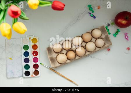 A vibrant and delightful setup for Easter egg painting featuring various brushes, beautiful flowers, and fresh apples Stock Photo
