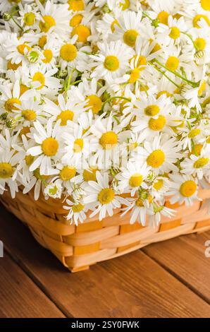Large beautiful bouquet of wildflowers daisies in a wicker basket on a wooden background close-up. Stock Photo