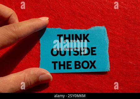 Think outside the box message written on ripped torn blue paper on red background. Conceptual think outside the box symbol. Copy space. Stock Photo