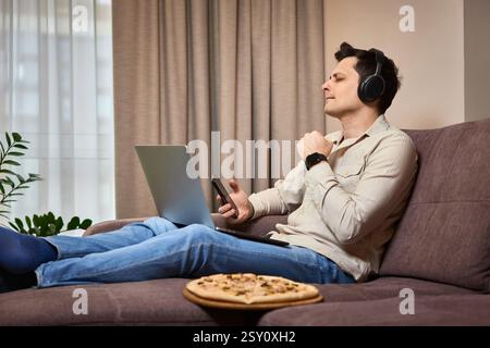 freelancer man using smart phone and laptop on sofa at home Stock Photo