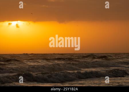 The sun peaks out from behind the clouds as it sets on the waves of the Gulf of Mexico. Stock Photo