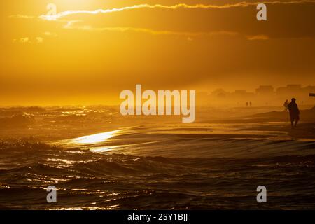A sunset shrouded in fog over the beach amidst turbulent waters along America's gulf coast. Stock Photo
