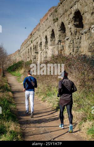 Two men runs and trains in the park of the ancient Roman aqueducts. Rome, Italy - January 26, 2019: two men run and train on the dirt path, in the public park. In the background the imposing ruins of the ancient Roman aqueduct. Roma RM Italy Copyright: xG.Leonardix Stock Photo