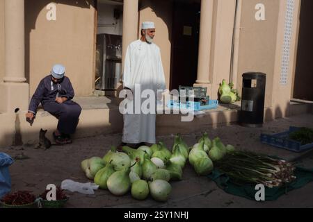 Omani Man Selling Gourds and Onions and Man Behind Playing with Kitten at Nizwa Market Oman Stock Photo