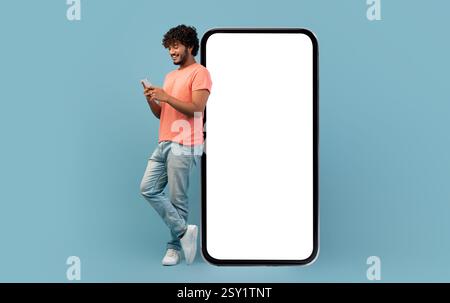 Cool indian guy leaning on huge smartphone, using cell phone Stock Photo