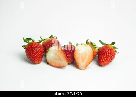 strawberries are arranged in a heart shape on a white background. The berries are red with green stems, some showing a transition to lighter, unripe a Stock Photo